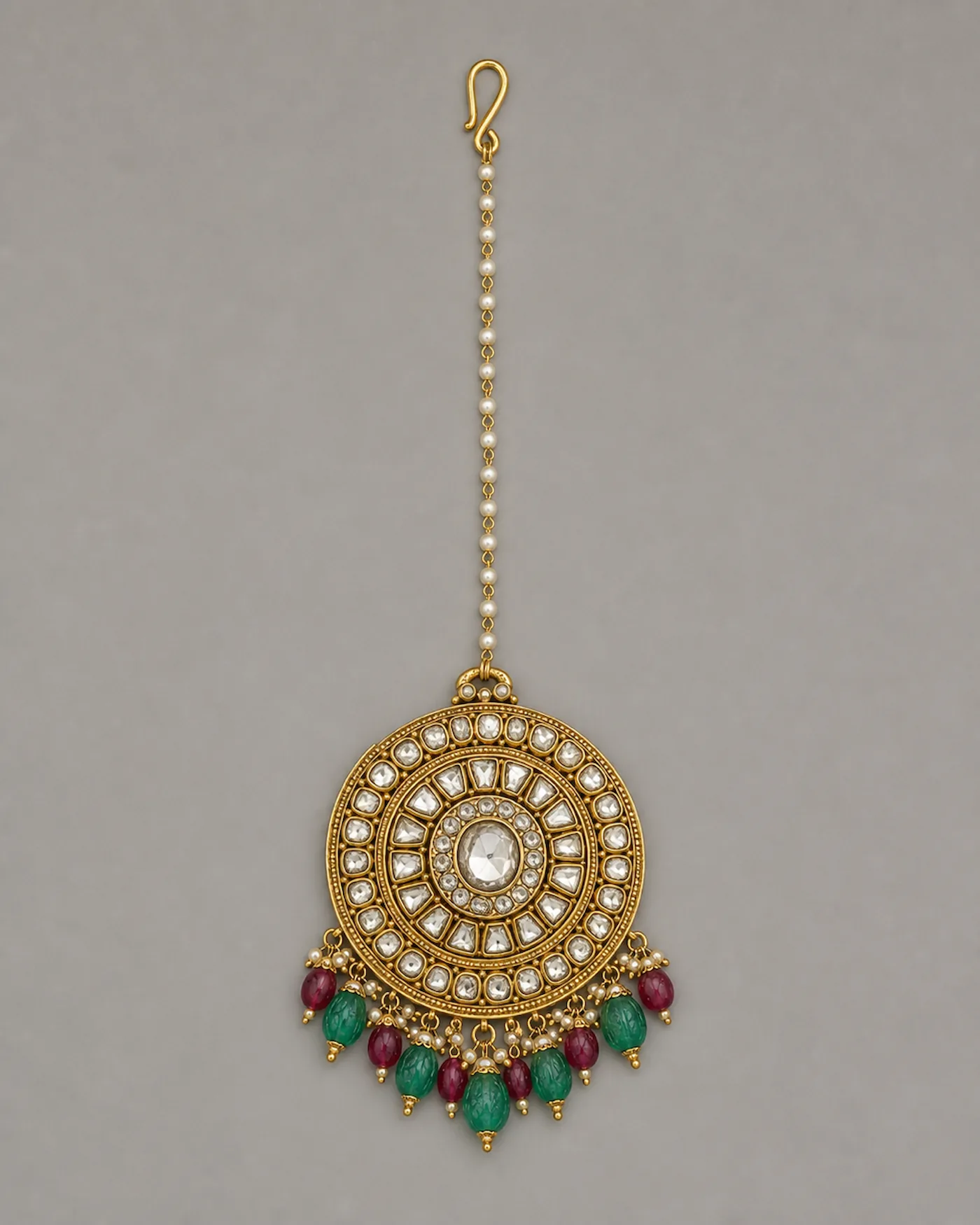 Bridal maang tikka: a kundan-set polki medallion hung with carved emerald and ruby drops, on a pearl and gold chain
