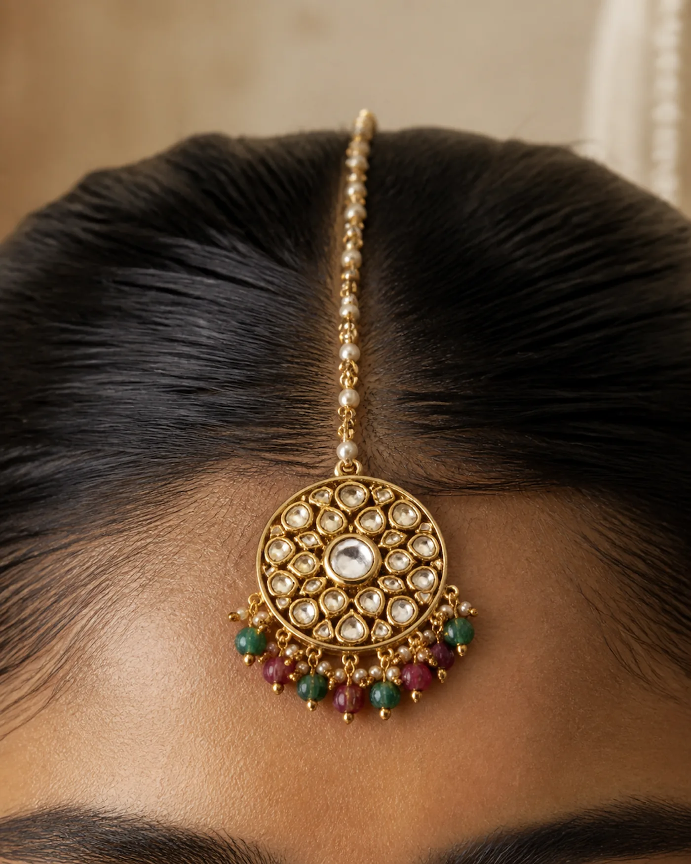 A bridal maang tikka resting at the hairline, its chain over the parting