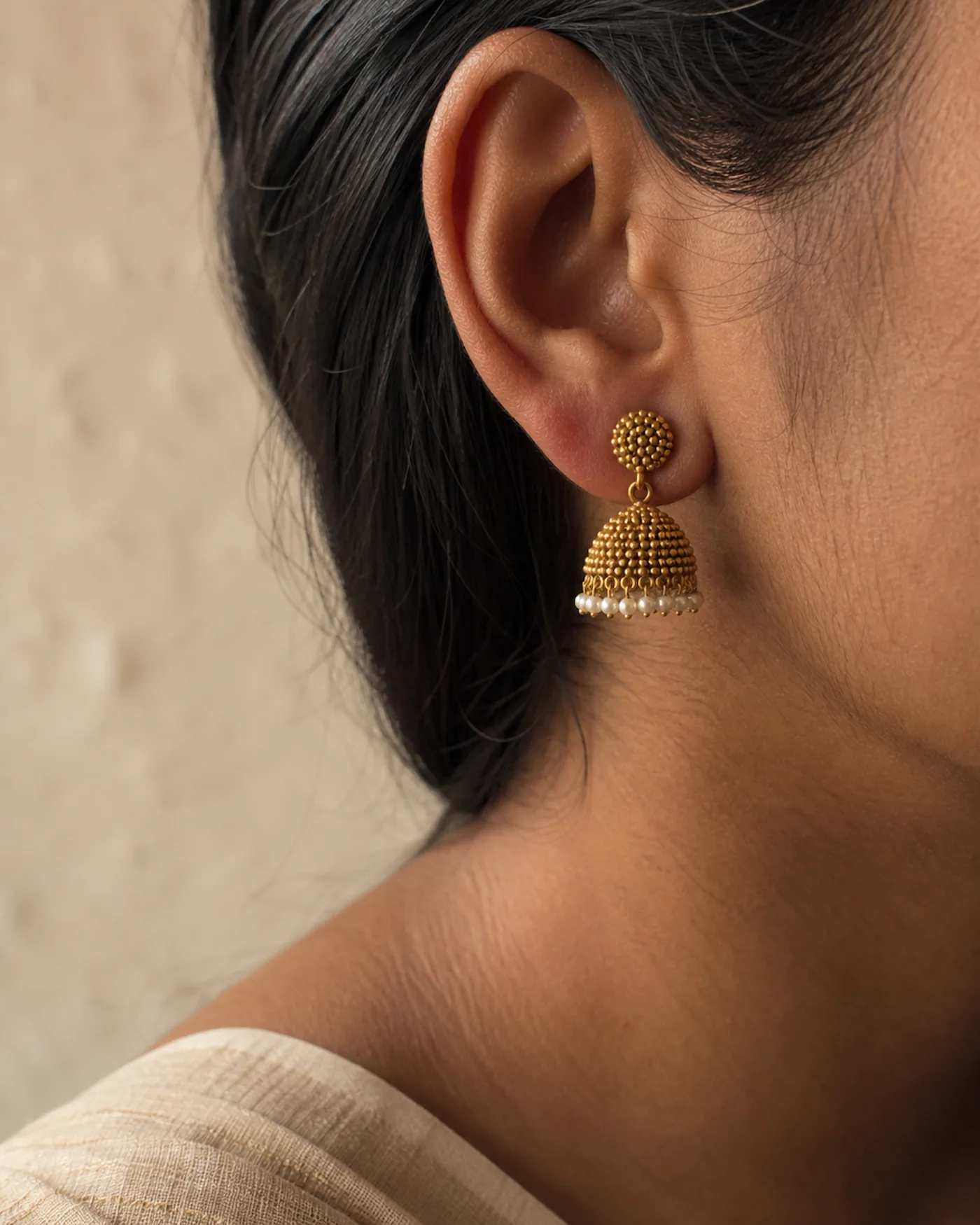 A small gold jhumka with a seed-pearl fringe, worn in the ear