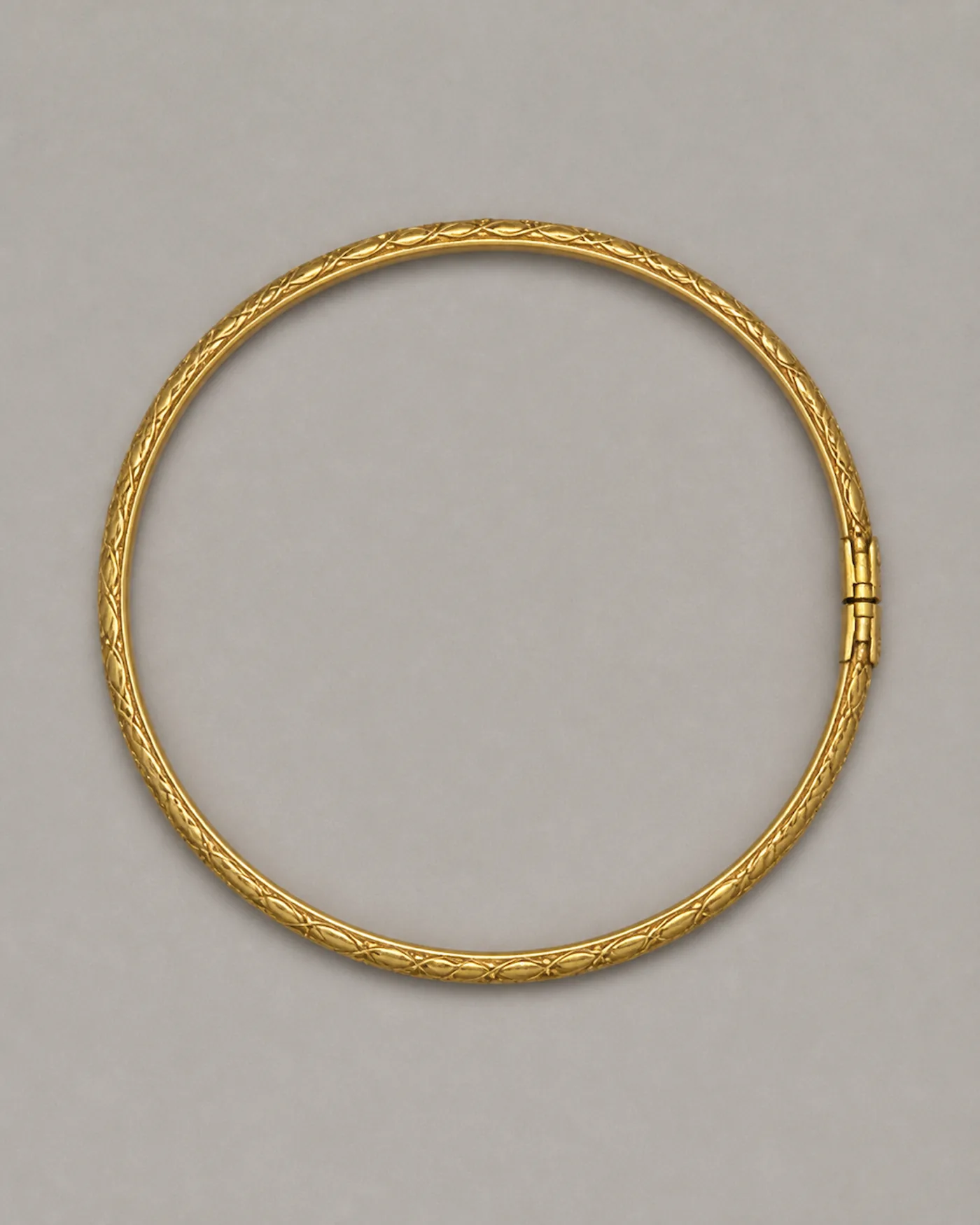Slim round gold kada chased all the way round with a fine vine pattern, closed by a plain hinged clasp