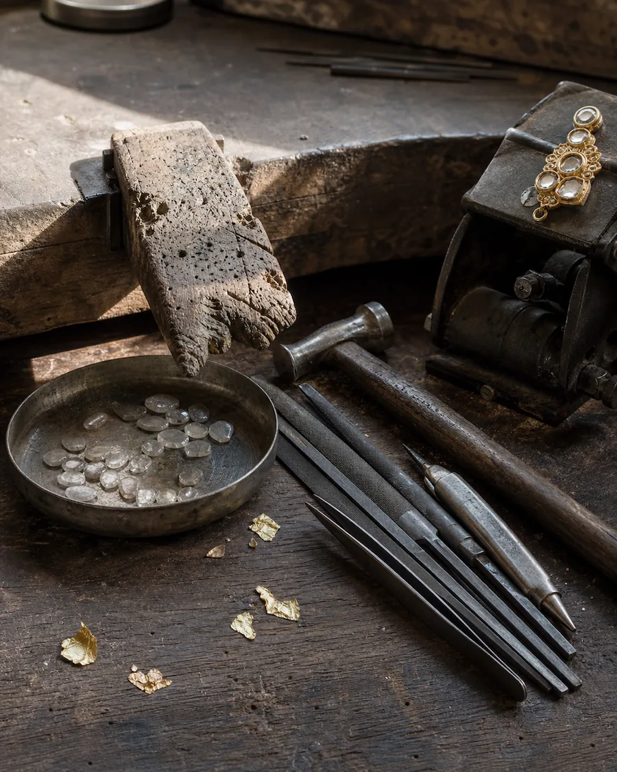 A jeweller's bench with a dish of uncut stones, files, tweezers and a part-finished gold pendant